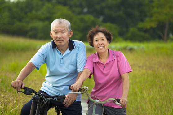 Happy Asian Seniors Couple Biking In Park.